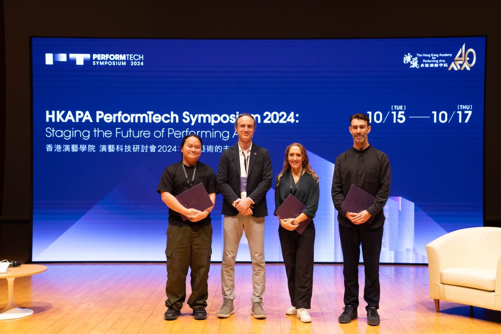 4 people standing on stage in Hong Kong  with a blue screen with the information about the the HKAPA PerformTech Symposium 